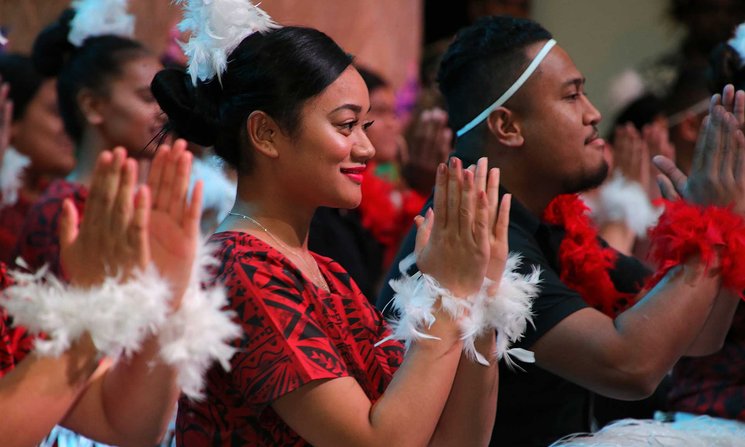 Close-up of person clapping while seated as part of a group giving a traditional Pacific performance